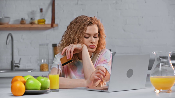 Γυναίκα συναρπαστικό κατά τη χρήση του φορητού υπολογιστή και της πιστωτικής κάρτας κοντά χυμό πορτοκάλι στο τραπέζι - Πλάνα, βίντεο