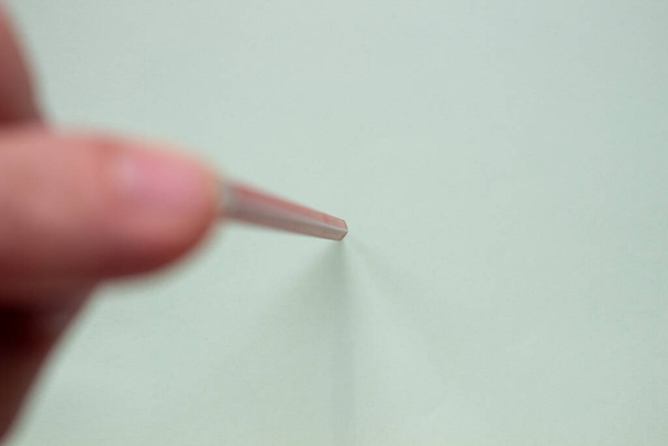 Ένας άντρας κρατά ένα κόκκινο μολύβι σε ένα ελαφρύ χαρτί με τα δάχτυλά του.. - Φωτογραφία, εικόνα