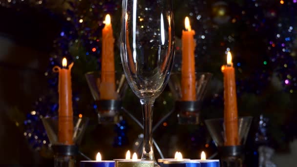 Christmas, New Year. An empty glass stands against the background of candles and colorful twinkling lights of a Christmas tree. Close up. - Metraje, vídeo