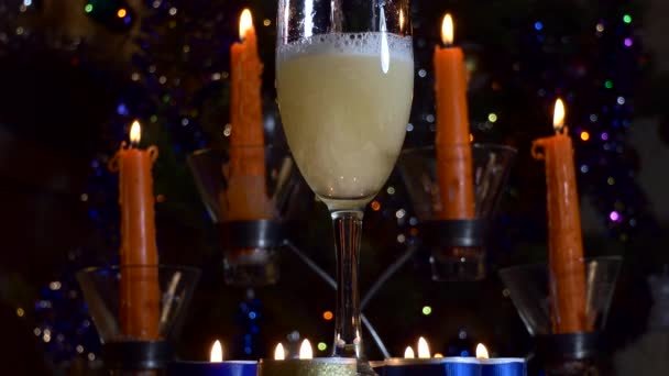Christmas, New Year. A stream of champagne is poured into a glass, which stands against the background of candles and flickering colored lights. Close up. - Кадры, видео