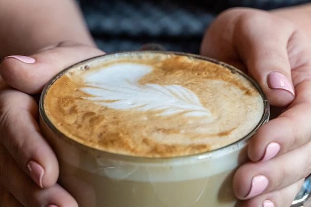 Closeup of woman hands hug a very big mug of cappucino with coffee art - Φωτογραφία, εικόνα
