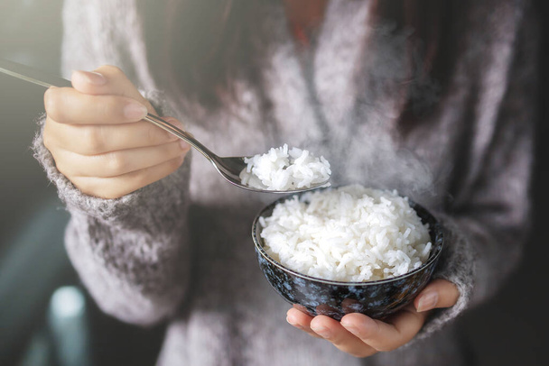 Asian women holding cooked jasmine rice bowls with spoon. Wearing a gray sweater. - Fotoğraf, Görsel