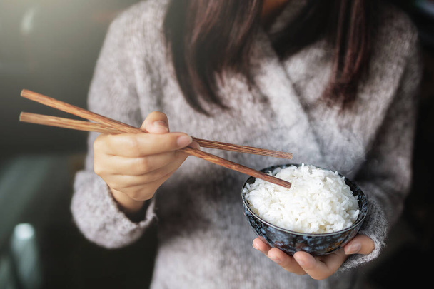 Asiatische Frauen halten gekochte Jasminreis-Schalen mit Essstäbchen in der Hand. Tragen eines grauen Pullovers. - Foto, Bild