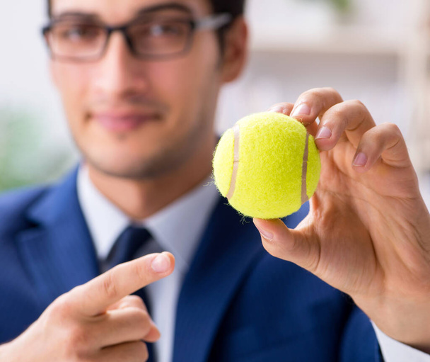 オフィスで働いているテニスボールを持つ若いビジネスマン - 写真・画像