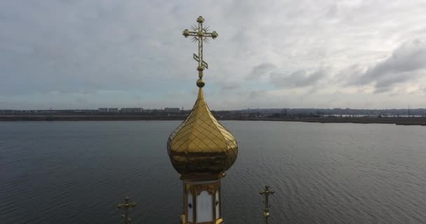 Luftaufnahme und Seitenansicht der goldenen Kuppel und des Kreuzes der kleinen Kirche am Flussufer vor dem Hintergrund der Stadt - Filmmaterial, Video