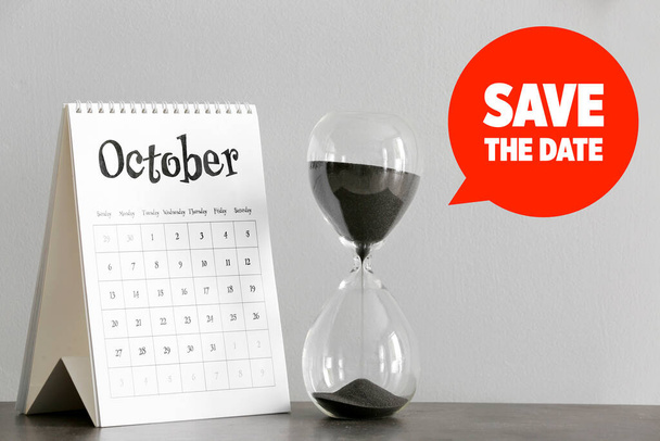 Ημερολόγιο με κλεψύδρα και κείμενο SAVE THE DATE σε γκρι φόντο - Φωτογραφία, εικόνα