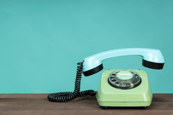 Eski telefon ahşap masada, yeşil arka planın önünde. Alıcısı kapalı eski bir telefon. Eski tarz fotoğraf.  - Fotoğraf, Görsel