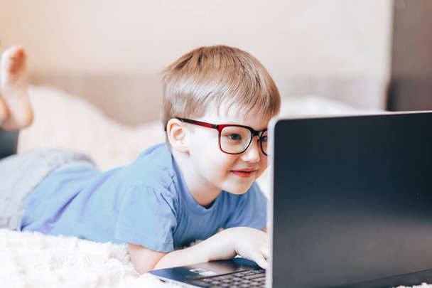 Μικρό χαρούμενο ξανθό αγόρι που χρησιμοποιεί φορητό υπολογιστή - Φωτογραφία, εικόνα
