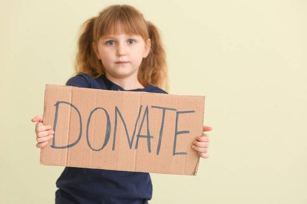 Little girl holding cardboard with text DONATE on color background - Photo, Image