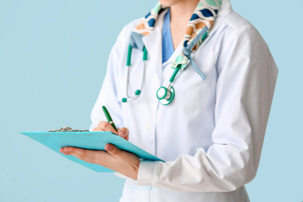 Female doctor with stethoscope and clipboard on color background, closeup - Foto, Imagen