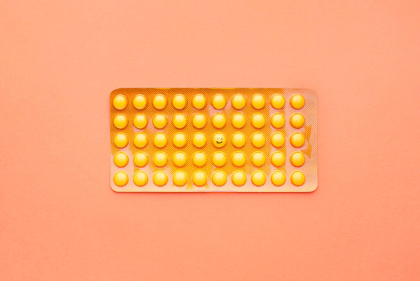 One pill with drawn happy face among yellow ones in blister pack on color background - Foto, immagini