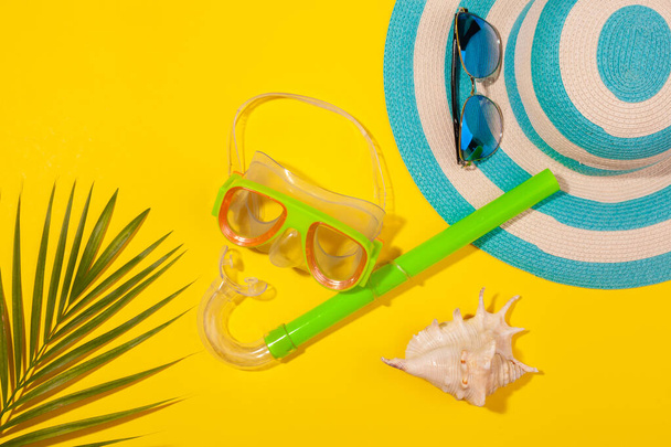 Top view on beach accessories on yellow background - sunglasses, striped blue hat, diving mask, sea shell and monstera leaf. Concept of the long-awaited vacation at sea and travel. Advertising space - Valokuva, kuva
