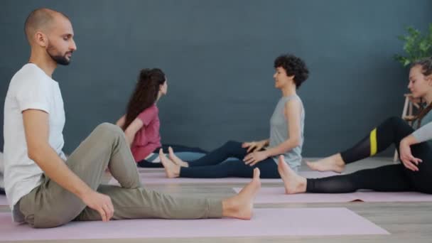 Girls and guy enjoying yoga practice in light room sitting on mats together - Video