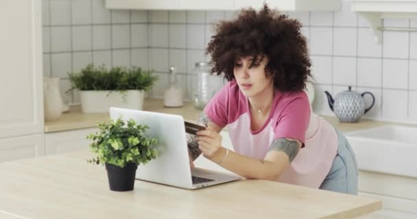 Menina fazendo pagamento on-line segurando cartão bancário usando laptop moderno em casa
. - Filmagem, Vídeo