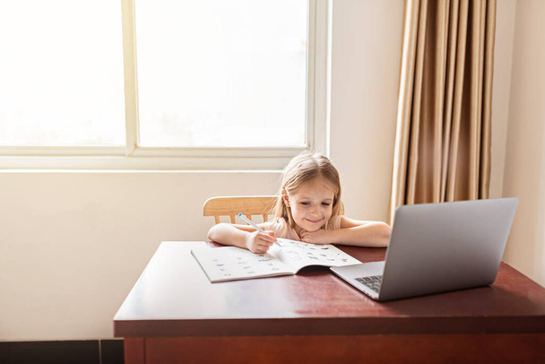 Pretty schoolgirl studying homework during her online lesson at home, social distance during quarantine covid-19, self-isolation, online education concept, home schooler. Workplace in living room - Foto, immagini