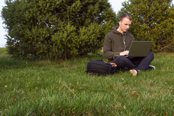 草の上に座ってノートパソコンで働く青年は - 写真・画像