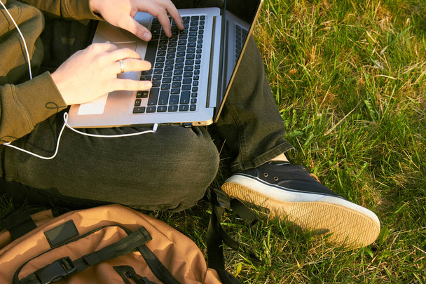 молодий чоловік працює в ноутбуці, сидячи на траві
 - Фото, зображення