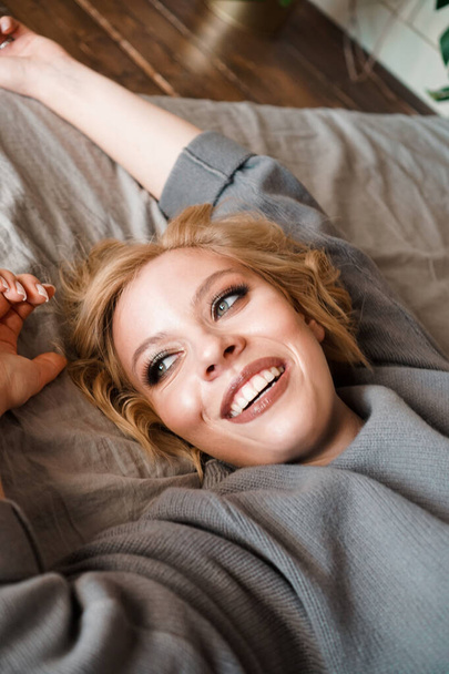 Belle jeune femme en pull gris riant couché au lit
 - Photo, image