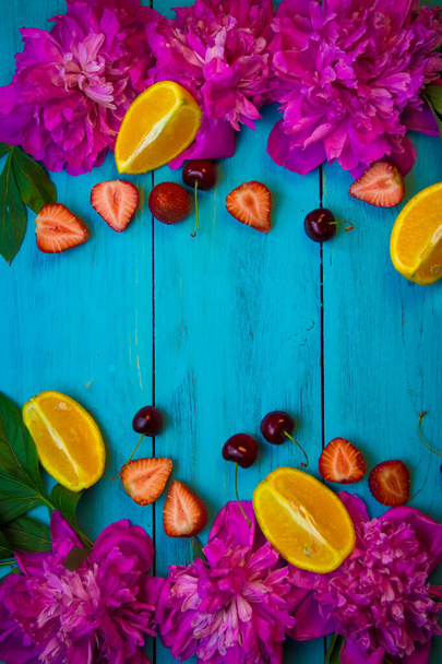 Tahta bir turkuaz arka planda pembe şakayık çiçekleri ve dilimlenmiş meyve uzanır. - Fotoğraf, Görsel