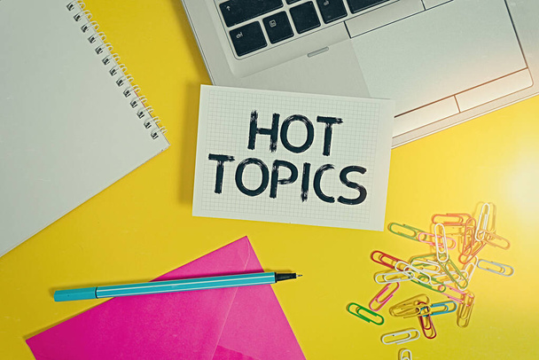 Writing note showing Hot Topics. Business photo showcasing subject that a lot of showing are arguing and discussing Laptop marker squared sheet spiral notebook envelope colored background. - Photo, Image
