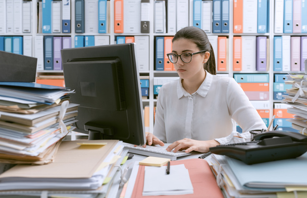 Молодая уверенная в себе деловая женщина, работающая в офисе, и куча бумажной работы
 - Фото, изображение