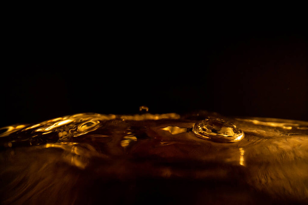 Water splash, gouden water splash geïsoleerd op zwarte achtergrond, water - Foto, afbeelding