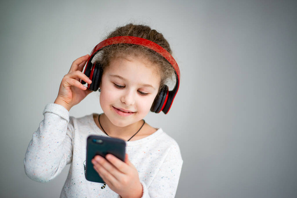 little girl in red headphones with a phone - Photo, Image