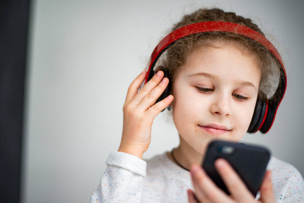 little girl in red headphones with a phone - Foto, Bild