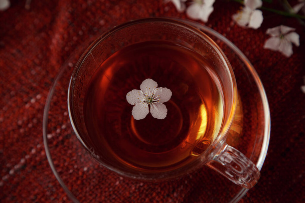 テーブルの上にお茶と桜の枝のカップ。美しい花と春の自然背景。赤い居心地の良い背景に桜のお茶と花。トップビュー、バナー。春のコンセプト - 写真・画像