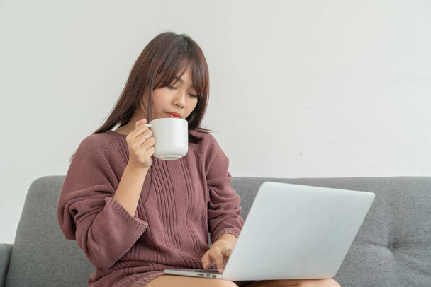 mooie aziatische vrouw met behulp van laptop op bank in woonkamer - Foto, afbeelding