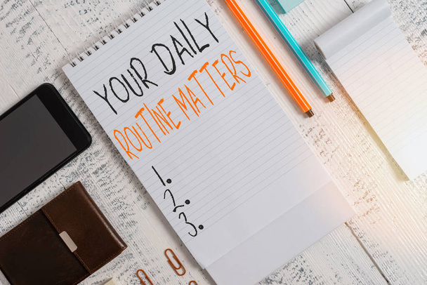 Handwriting text Your Daily Routine Matters. Concept meaning practice of regularly doing things in fixed order Smartphone man wallet clips notebook pens ballpoints note pad wooden table. - Photo, Image