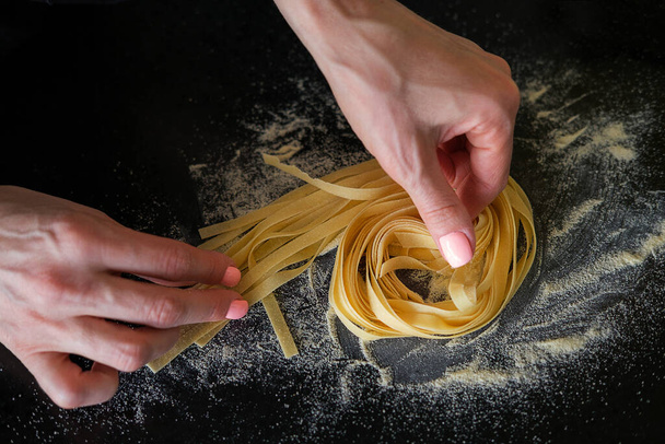 Preparation of homemade pasta. The cook turns the nest out of the paste on a black stone background - Foto, imagen