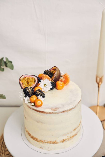 A white cake with berries and passionfruits with plants behind a white background - Foto, Imagen