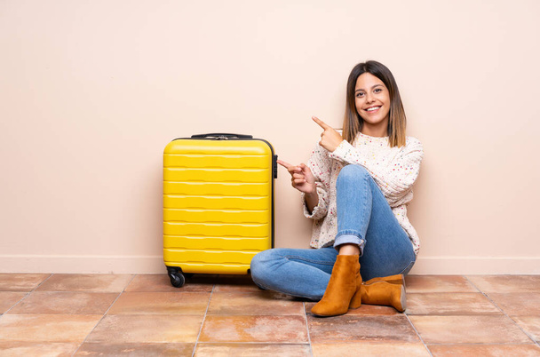側に指を指して床に座ってスーツケースを持つ旅行者の女性 - 写真・画像