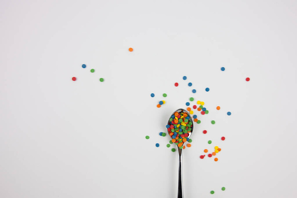 Multi-colored sweets in an iron spoon on a white background - Foto, Bild