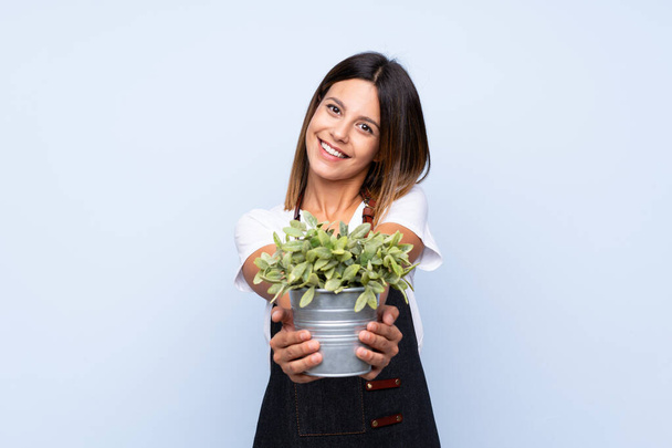 Young woman over isolated blue background taking a flowerpot - Foto, Imagen