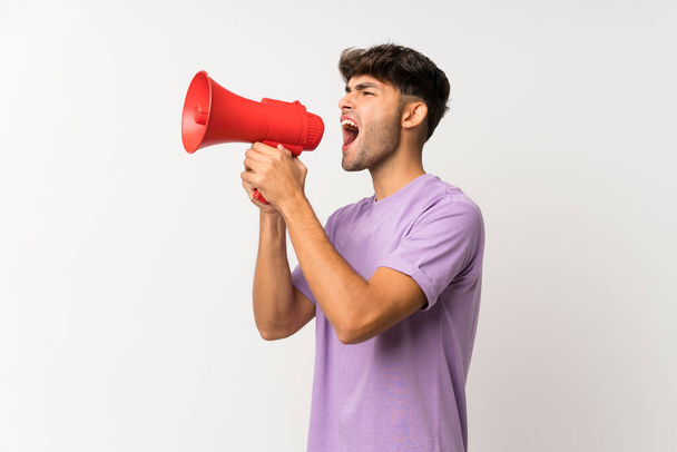 Молодий красивий чоловік над ізольованим білим тлом кричить через мегафон
 - Фото, зображення