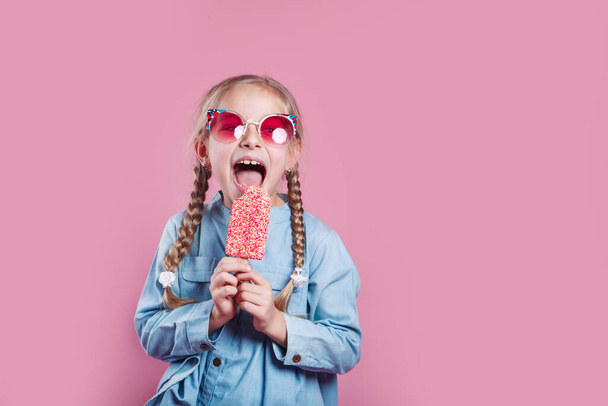 kis vidám lány napszemüvegben fagylalt rózsaszín háttér - Fotó, kép