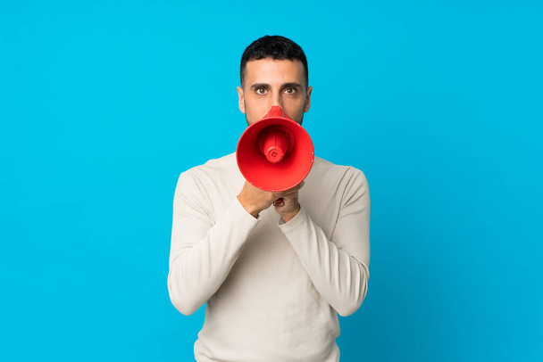 Young man over isolated blue background shouting through a megaphone - Photo, Image