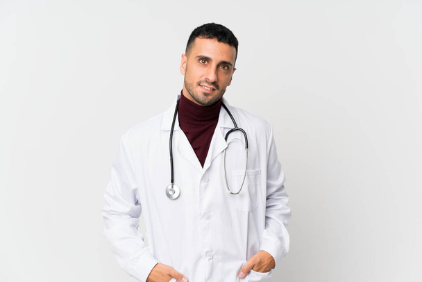 Mladý muž přes izolované bílé pozadí s lékařem šaty - Fotografie, Obrázek