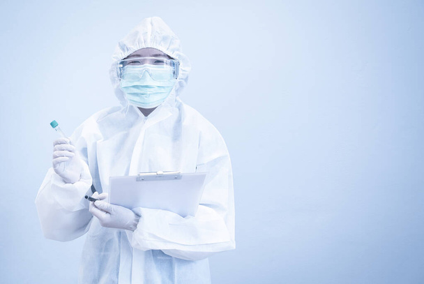 Asiatischer Arzt in persönlichem Schutzanzug mit Reagenzglas, Maske und Patiententabelle, arbeitet hart ohne Depressionen in der Krise des Covid-19. Medizin- und Gesundheitskonzept. - Foto, Bild