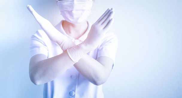 Woman nurse wearing mask raise hands cross as a sign, to prohibit people from leaving the house, prevent spreading of coronavirus outbreak. Stay at home and social distancing concept. - Photo, image