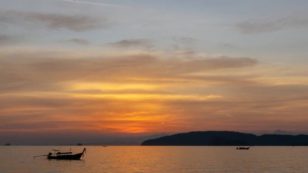 Gyönyörű táj naplemente ragyogó narancssárga fény festett felhős ég vált alkonyat hajnalban, a tenger felett, hosszú farok csónak és fekete hegy, esti idő a strandon Krabi, Thaiföld - Fotó, kép