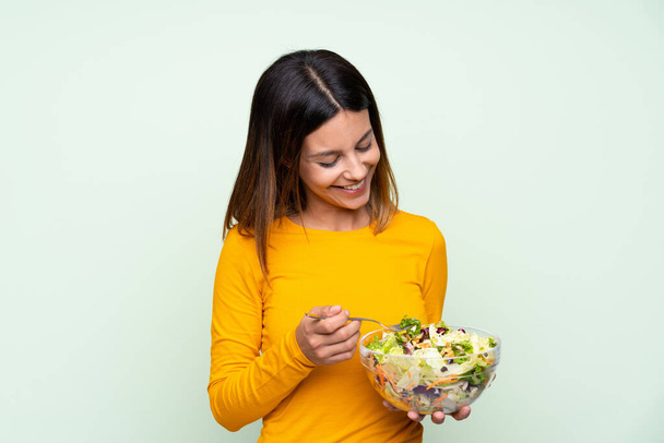 Mladá žena se salátem na izolované zelené stěně - Fotografie, Obrázek