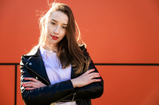 Spring portrait of a smiling beautiful girl with emotions in the sun outdoors on an orange background. Model is wearing a white blouse and a jacket in front of the camera - Foto, immagini
