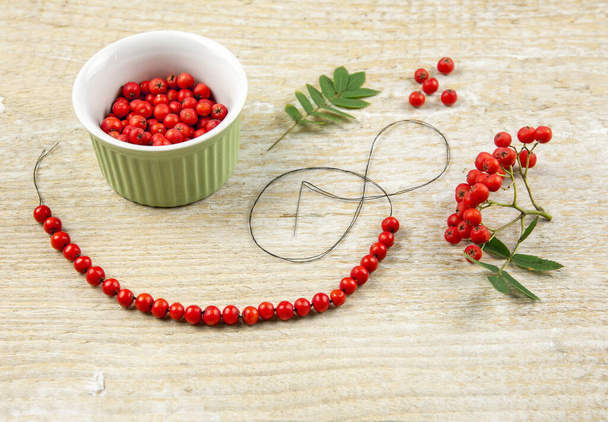 Making protective rowan berry charm necklace, it is believed that rowan tree berries have magical properties. Old folklore concept. Light natural wooden background. - Photo, Image
