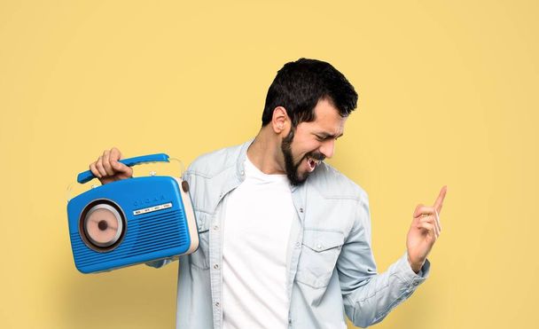 Knappe man met baard met een radio over geïsoleerde gele achtergrond - Foto, afbeelding