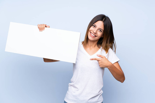 Giovane donna su sfondo blu isolato con un cartello bianco vuoto per inserire un concetto
 - Foto, immagini