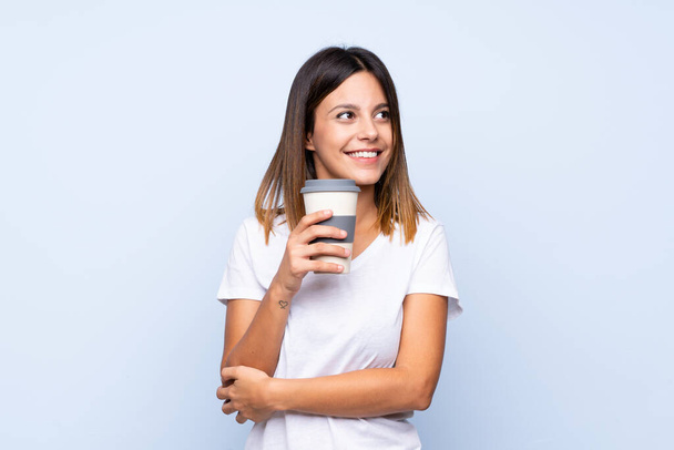 Молодая женщина на изолированном синем фоне держит кофе, чтобы забрать
 - Фото, изображение