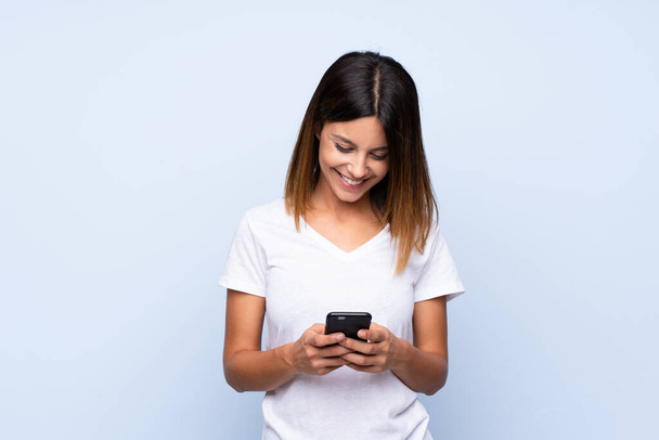 Молода жінка над ізольованим синім тлом надсилає повідомлення або електронну пошту з мобільним телефоном
 - Фото, зображення